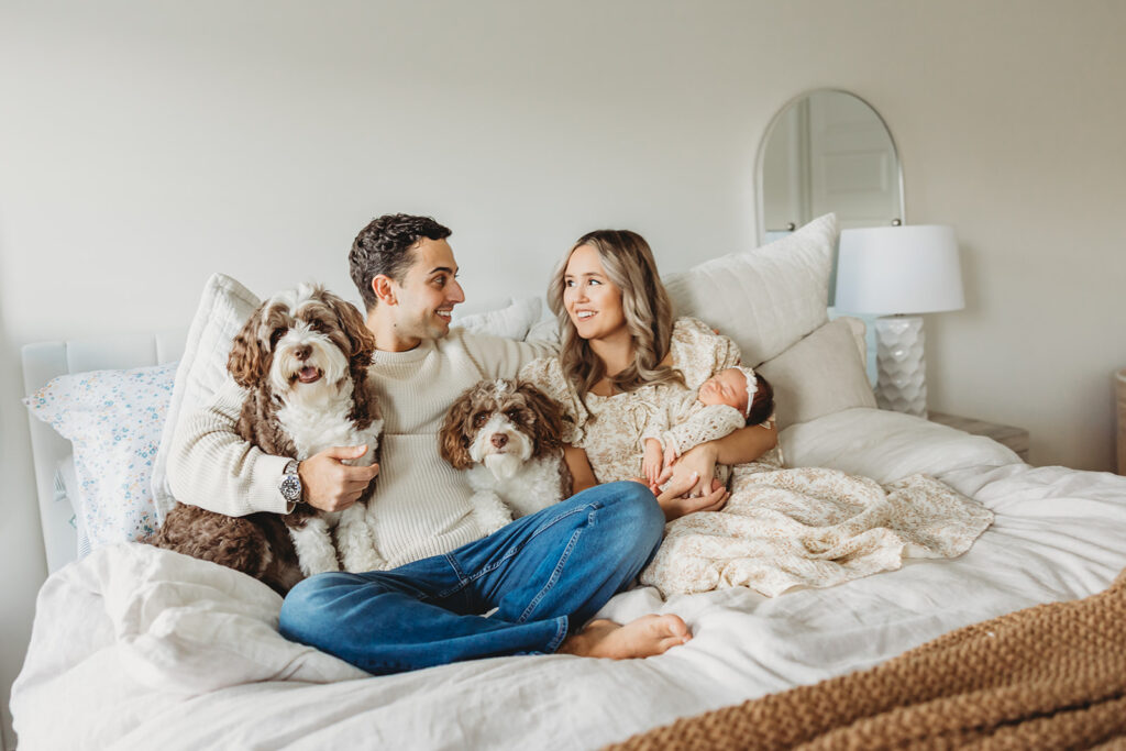 Lifestyle newborn session with parents, newborn, and dogs on bed during in-home photography session