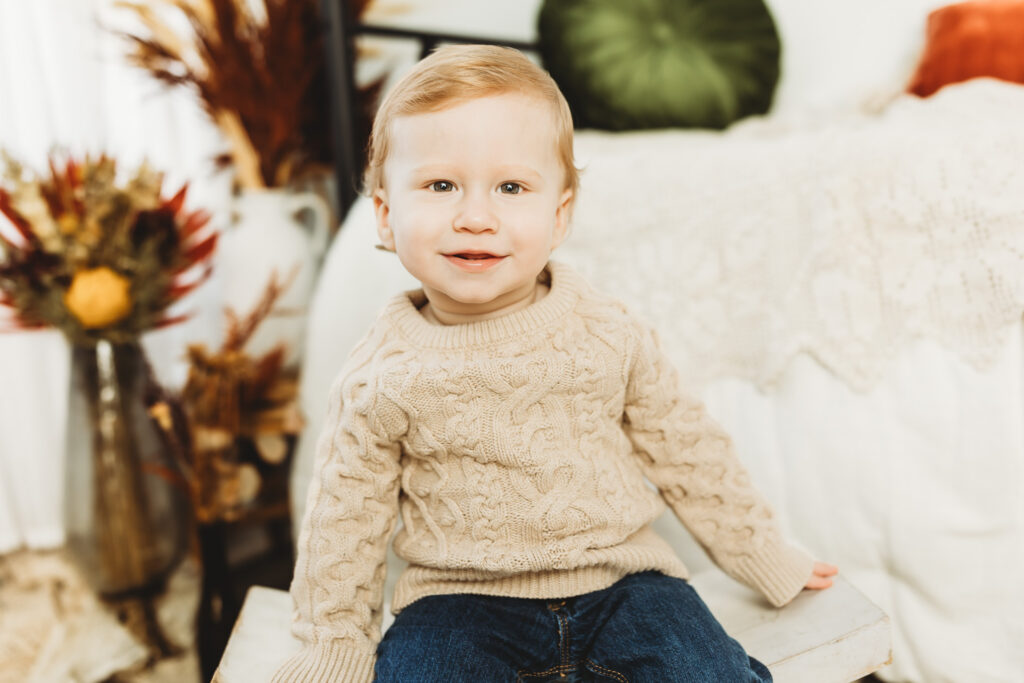 Little one year old boy smiling in a sweet cable knit sweater for his first birthday photo. 