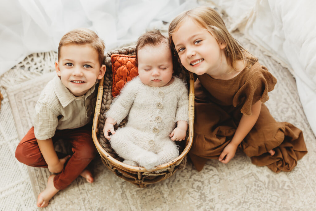 Brother, baby, and sister posing together for a sweet family newborn photo. 