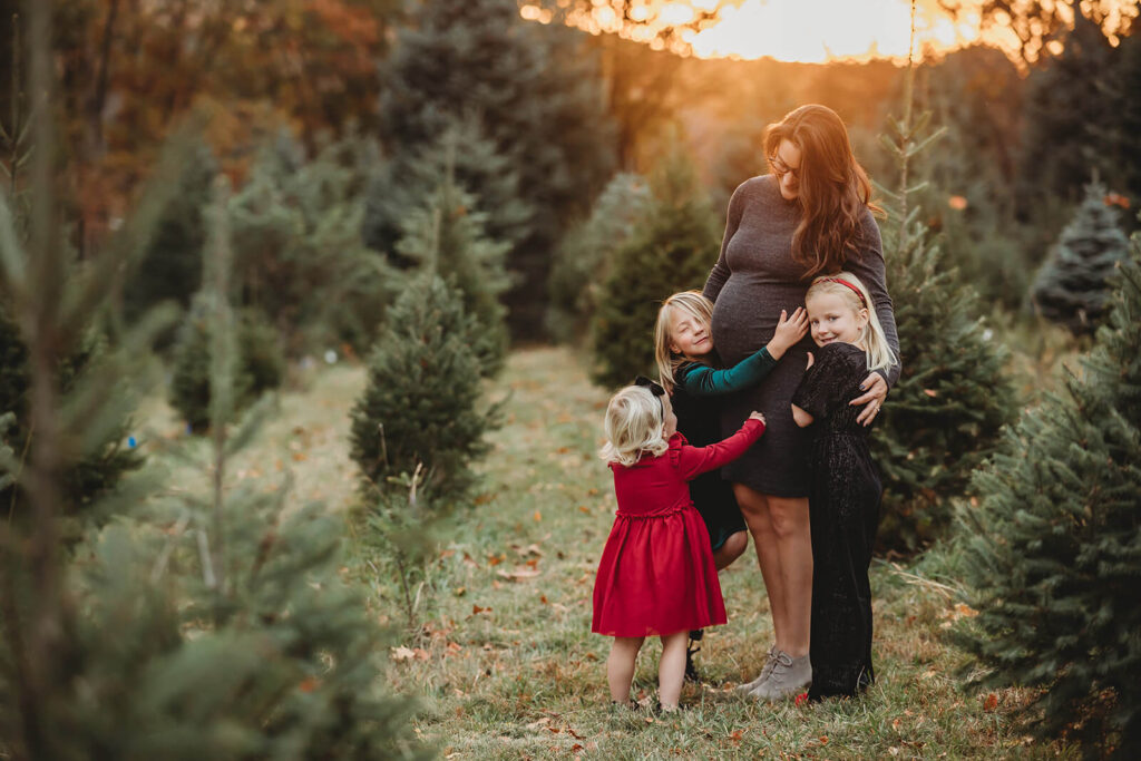 Pregnant mom and daughters hugging at a Christmas Tree Farm around Harrisburg 