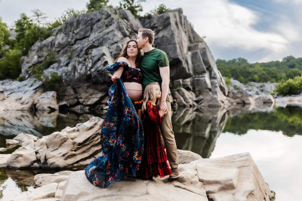 Husband kissing pregnant mother with beautiful toddler child in scenic outdoor setting Potomac MD