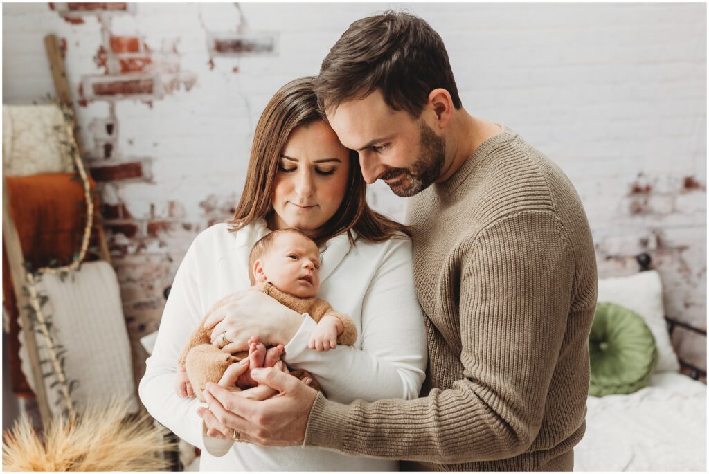 Parents standing close together holding their newborn baby and admiring him during their newborn session