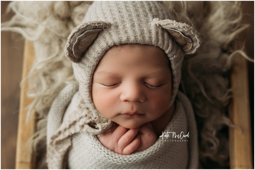 baby boy swaddled in tan with a bear ear bonnet on sleeping during his newborn session