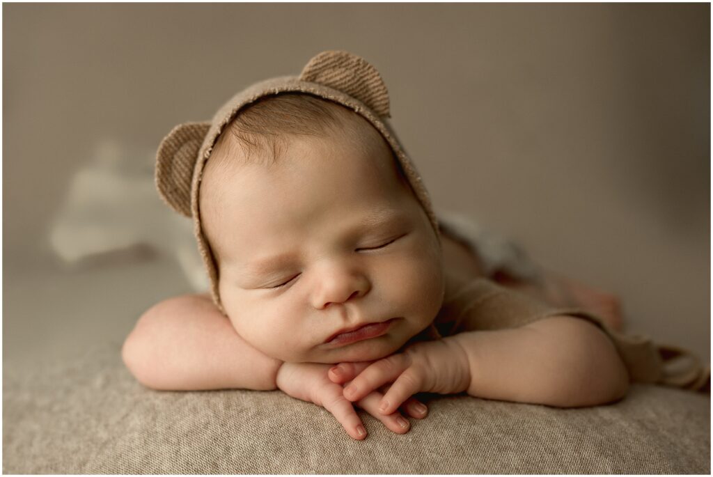 Newborn session with baby boy with his head on his heads wearing a tan bonnet with bear ears 