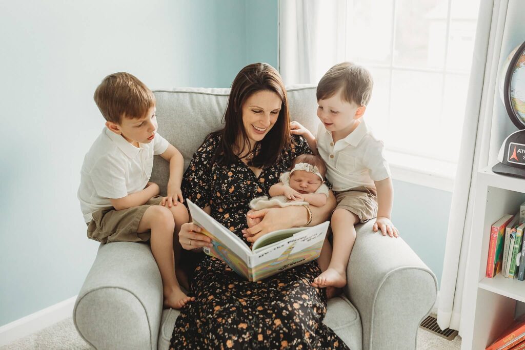 Mom and her three children sitting together reading a book. 