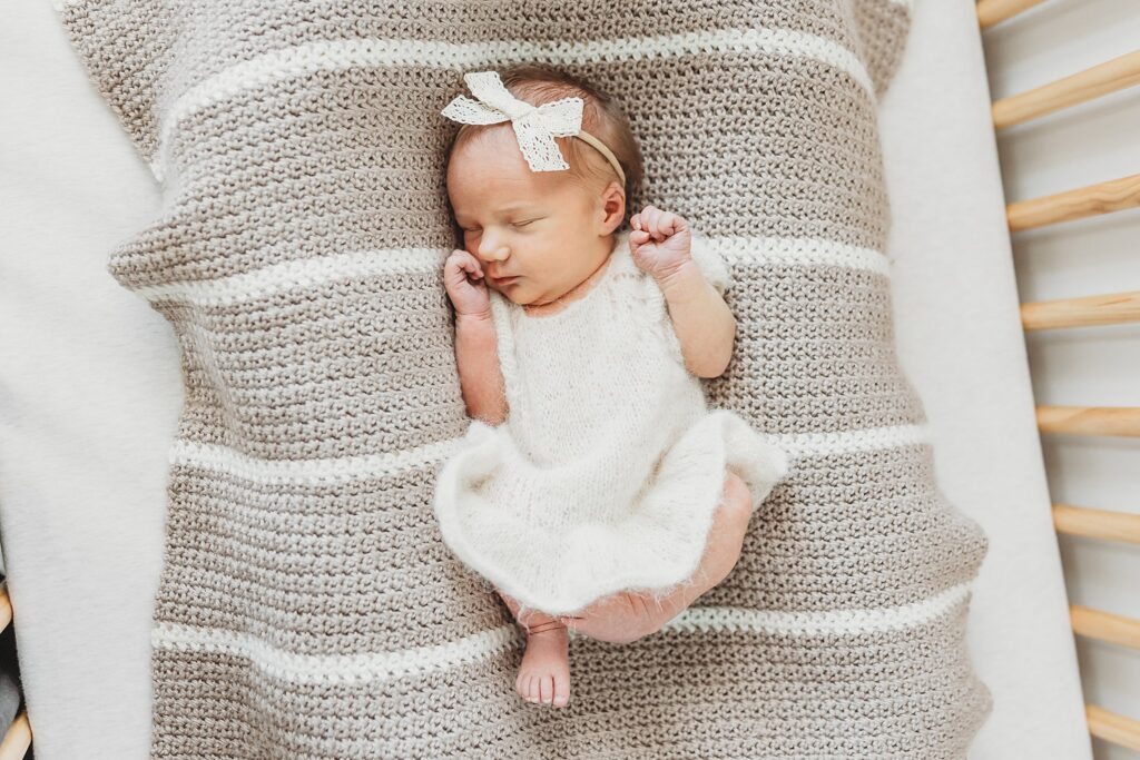 Newborn baby girl snuggled in bed with a lace bow 