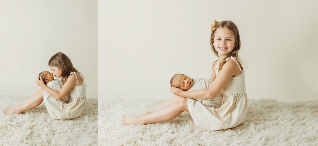 Big sister in cream dress holding newborn baby brother wrapped in cream swaddle