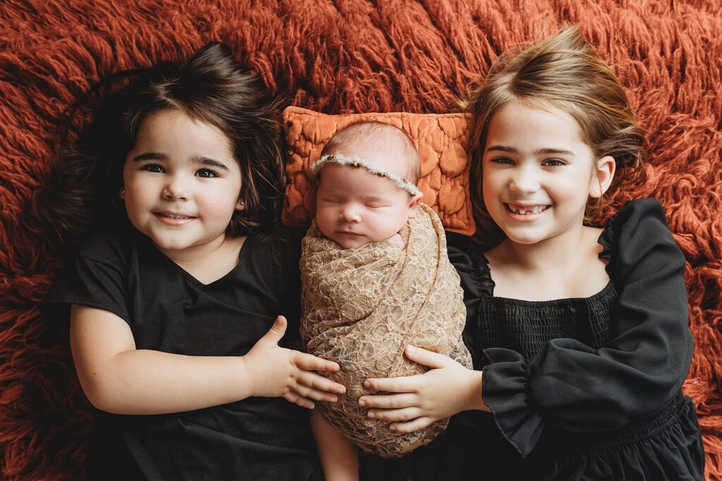 Three sisters smiling for newborn baby girl photos