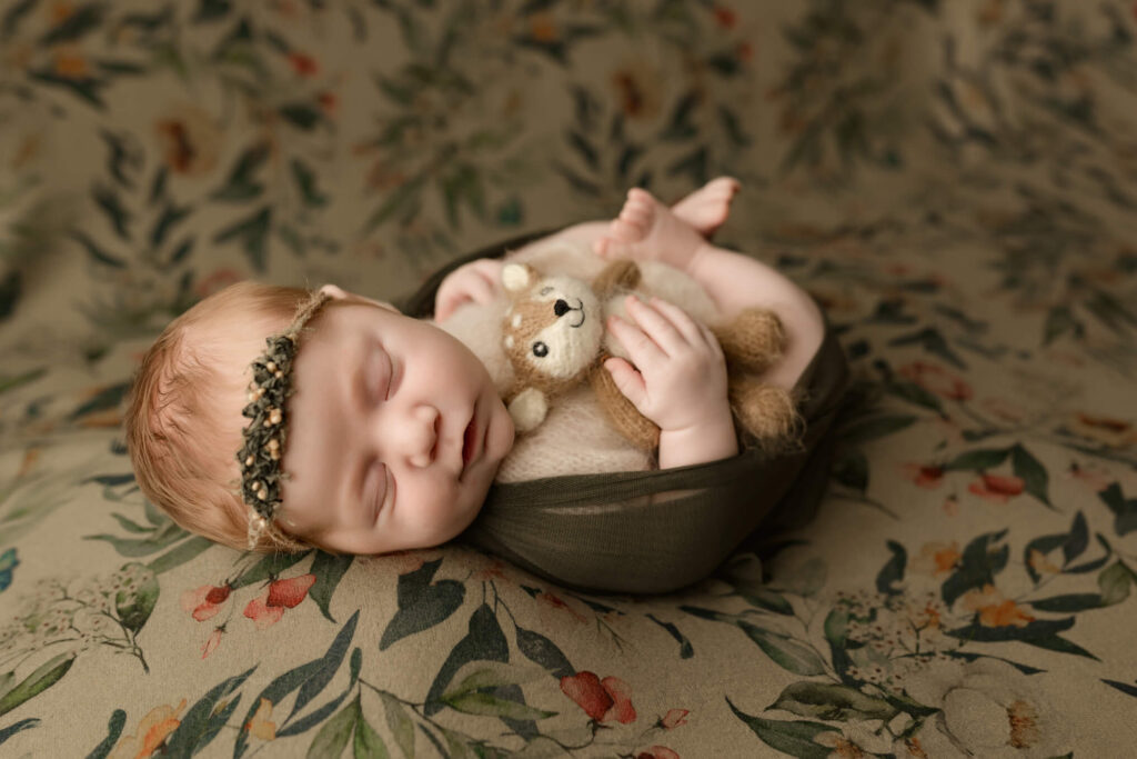 Baby girl swaddled in a sheer olive green swaddle holding a tiny deer stuffy with a delicate head band during her york, pa studio newborn session