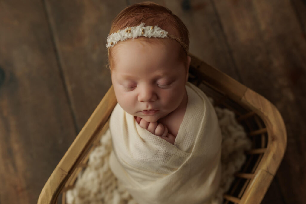 Newborn baby girl sleeping swaddled in a basket with a sweet white headband