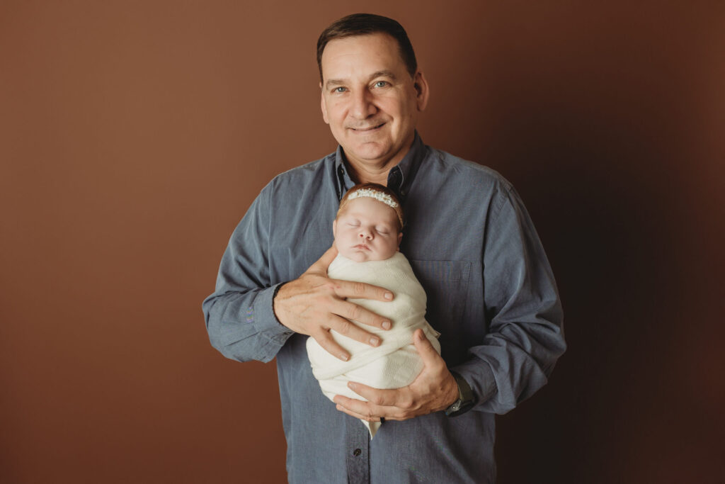 Proud dad holding his newborn baby girl wrapped in a soft white swaddle during their newborn photos in york pa