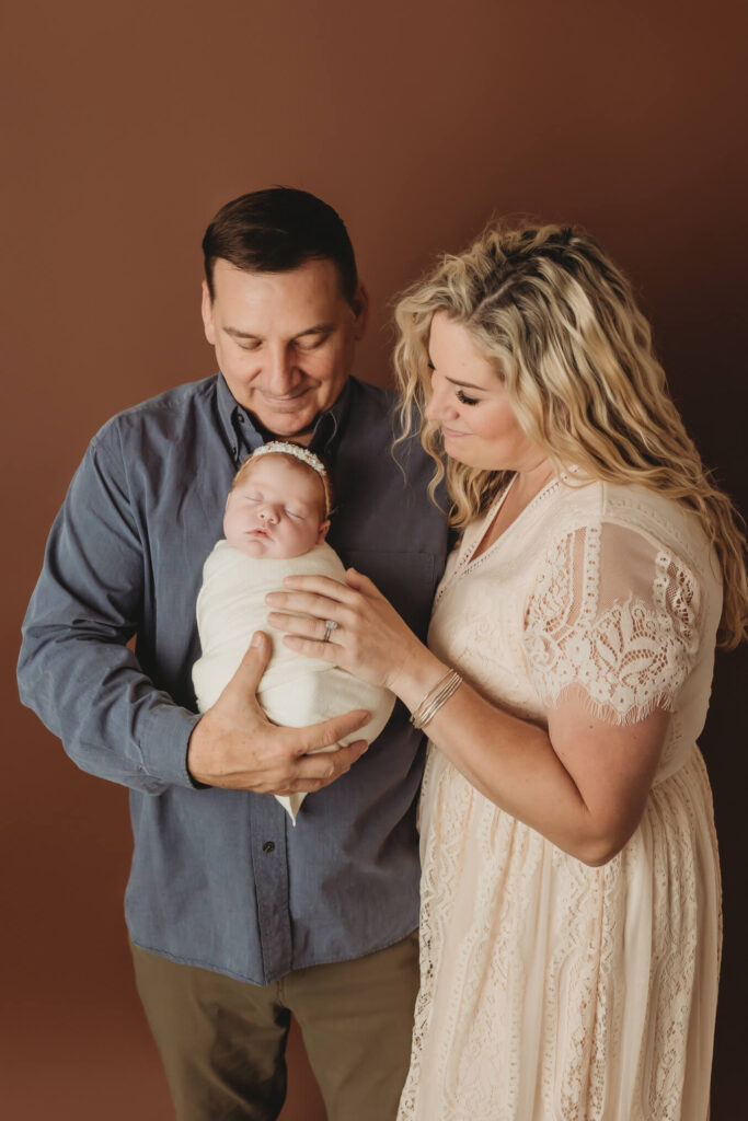 Mom and dad looking adoringly at their newborn baby swaddled sweetly during their family newborn session