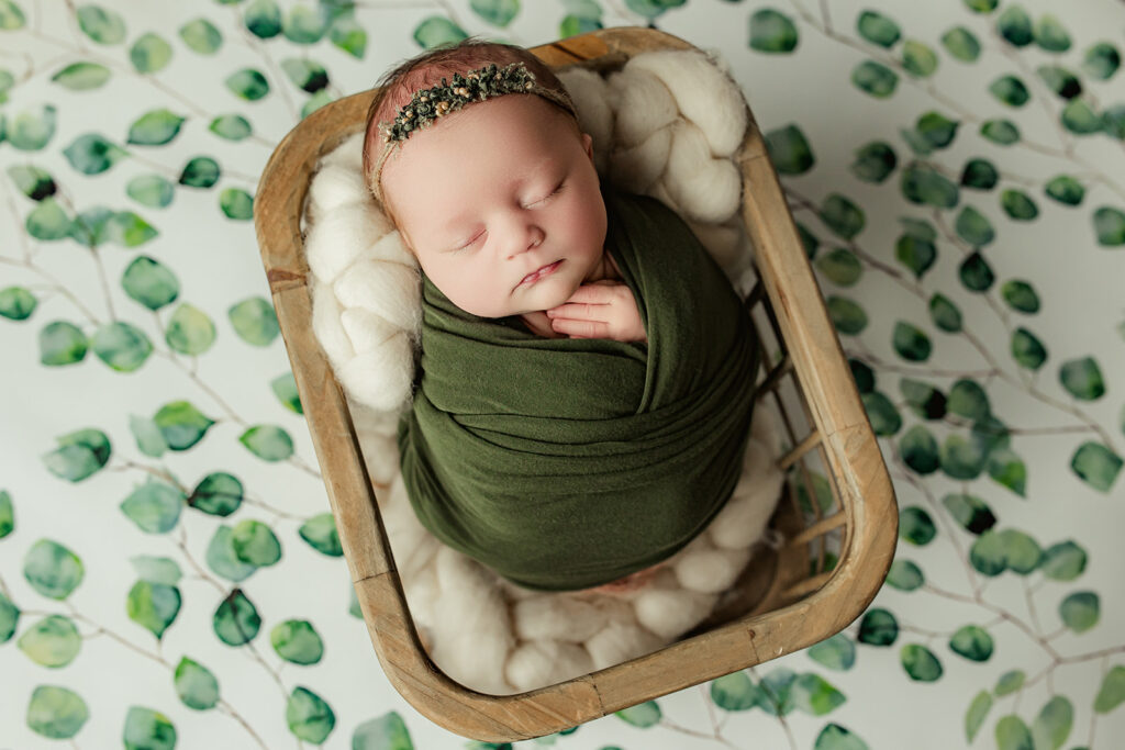 Baby girl swaddled in a green wrap on a green foliage backdrop