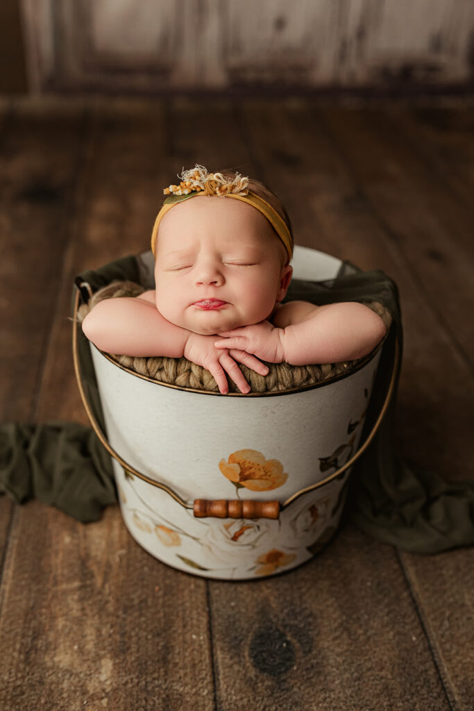 Newborn baby asleep in a bucket with a pouty face 