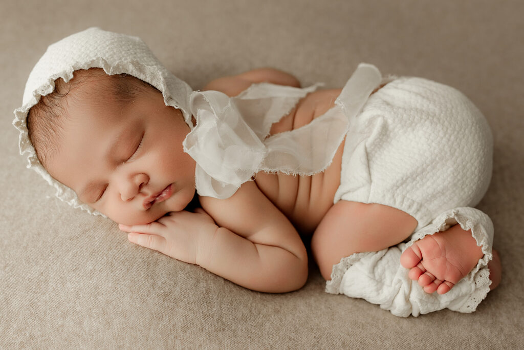 Mechanicsburg newborn baby girl in a cream bonnet sleeping on a tan background 