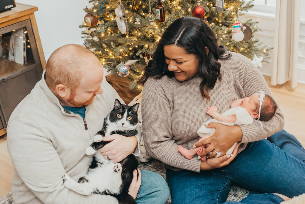 New parents in front of the Christmas tree holding their newborn baby girl and their tuxedo cat in their Hershey home around the holidays
