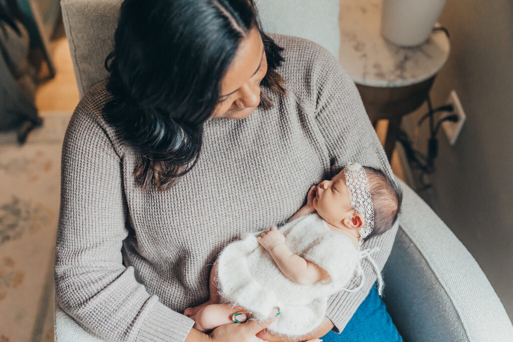 Mom looking down at her newborn baby girl in a cream outfit with a coordinating cream lace headband