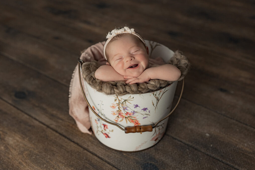 baby girl smiling posed in a bucket during studio newborn