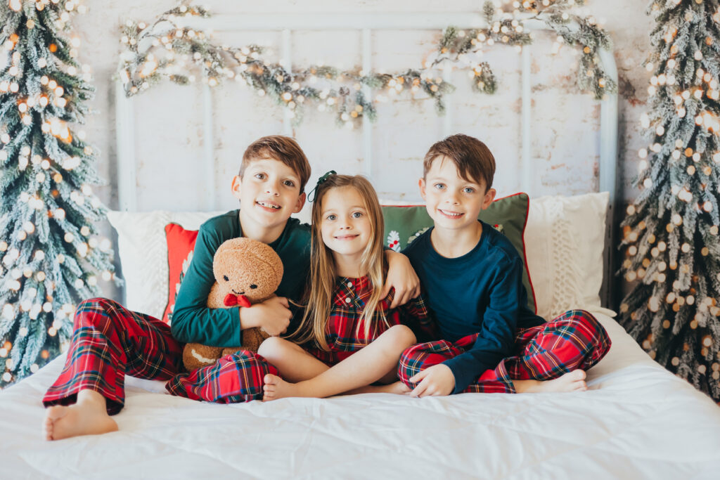brothers and their sister pose smiling in their matching christmas pajamas for their mechanicsburg christmas mini session