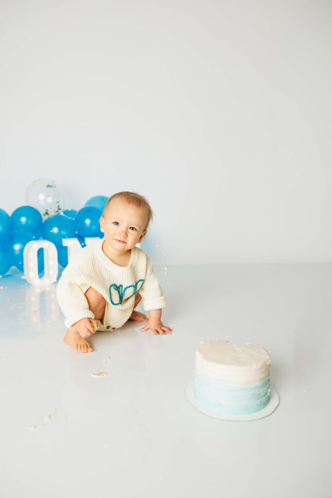 Baby boy squatting on the floor in front of a simple blue and white ombre birthday cake