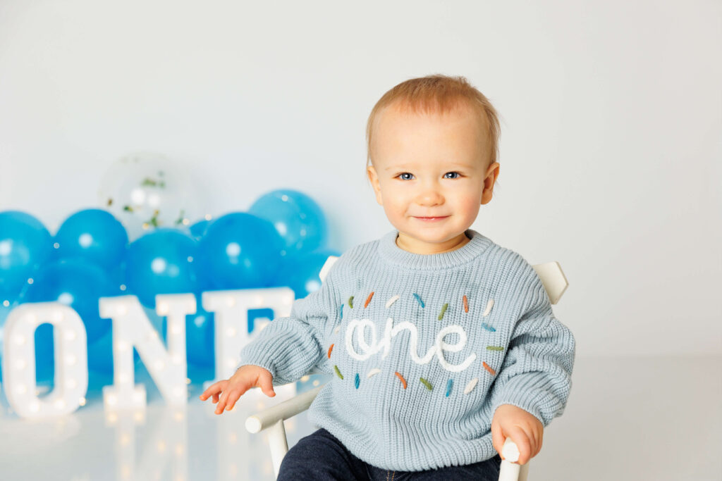 Little toddler boy smiling in a confetti one sweater for his first birthday photos 