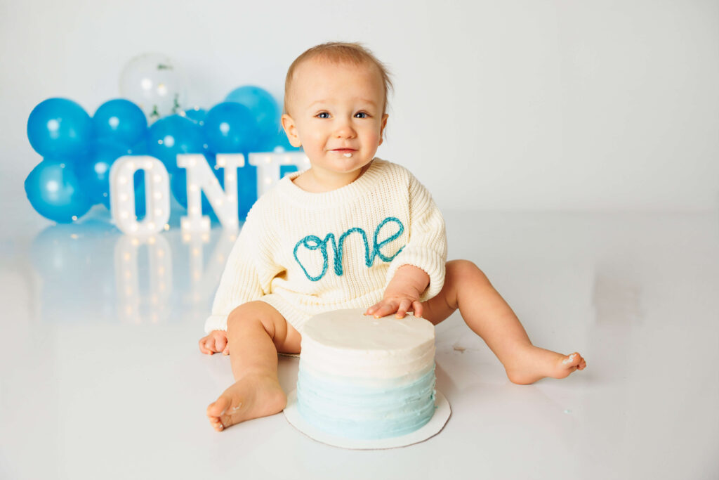 One year old boy with a simple cake on the floor in front of him with his hand on his cake 