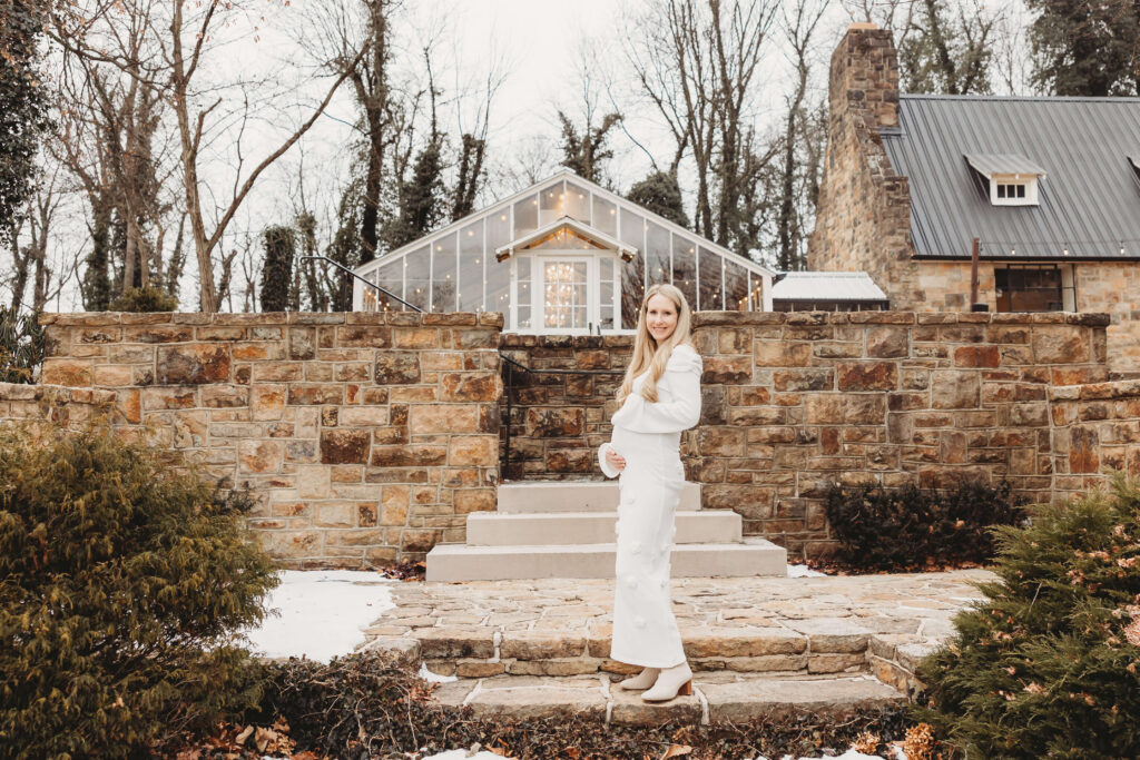 Side profile of expectant mother posing in front of the stone wall and greenhouse during a York maternity session in late winter.
