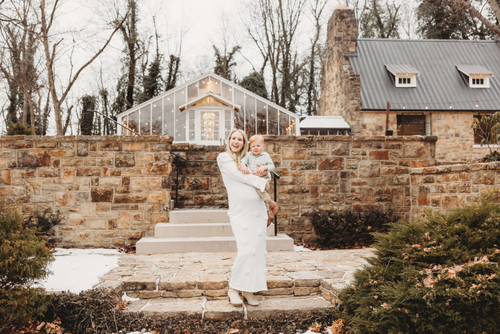 Mother holding her one year old son on the stone steps with the greenhouse glowing behind them at Historic Shady Lane.