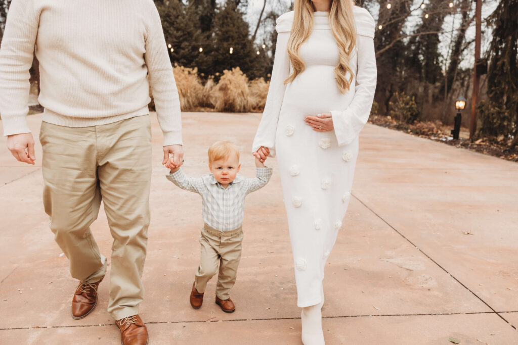 Parents holding hands with their toddler son as they walk outdoors during a winter maternity session at Historic Shady Lane in York County.