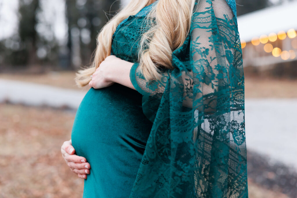 Close up detail of pregnant belly in a green lace gown during a winter maternity session at Historic Shady Lane in Manchester, PA.