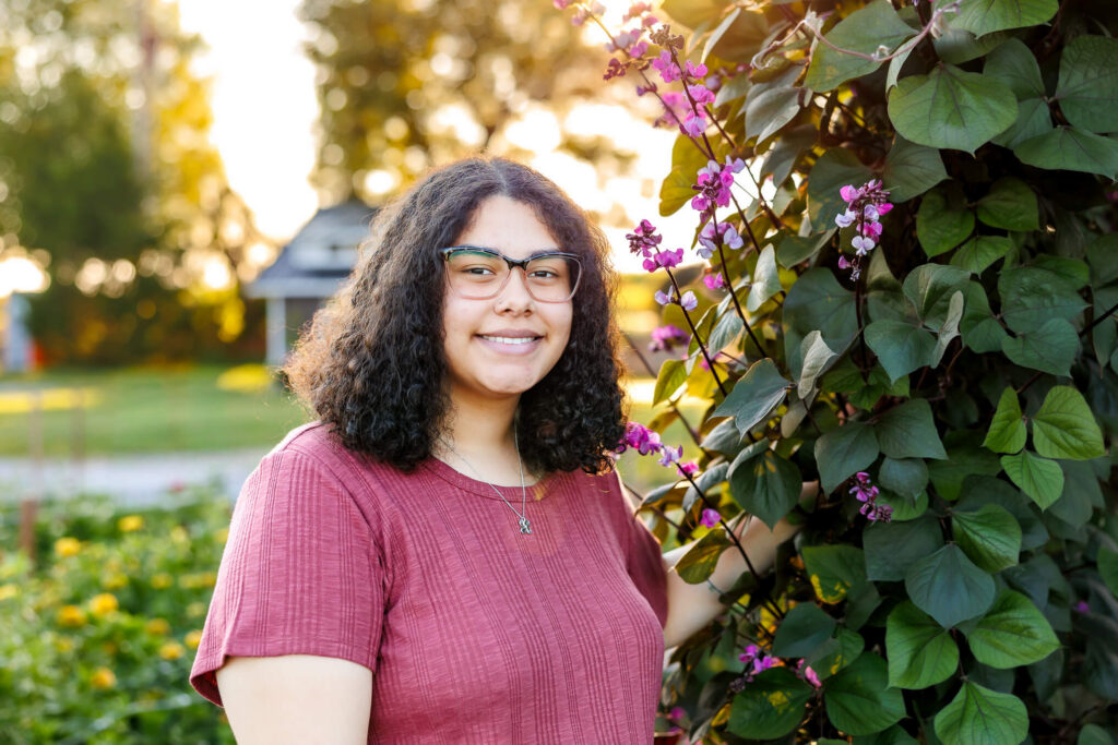 Senior girl posing beside purple flowers during a golden hour Central PA senior session at Royal Oaks Farm in Lebanon PA