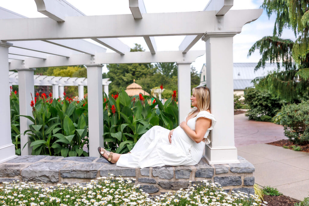 Expecting mom in a white dress beneath a pergola during her Hershey Gardens maternity photos.