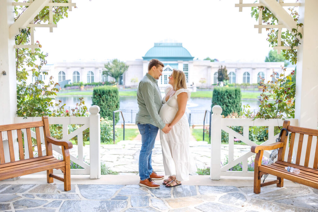 Expecting couple holding hands beneath a garden pavilion during their outdoor maternity session.