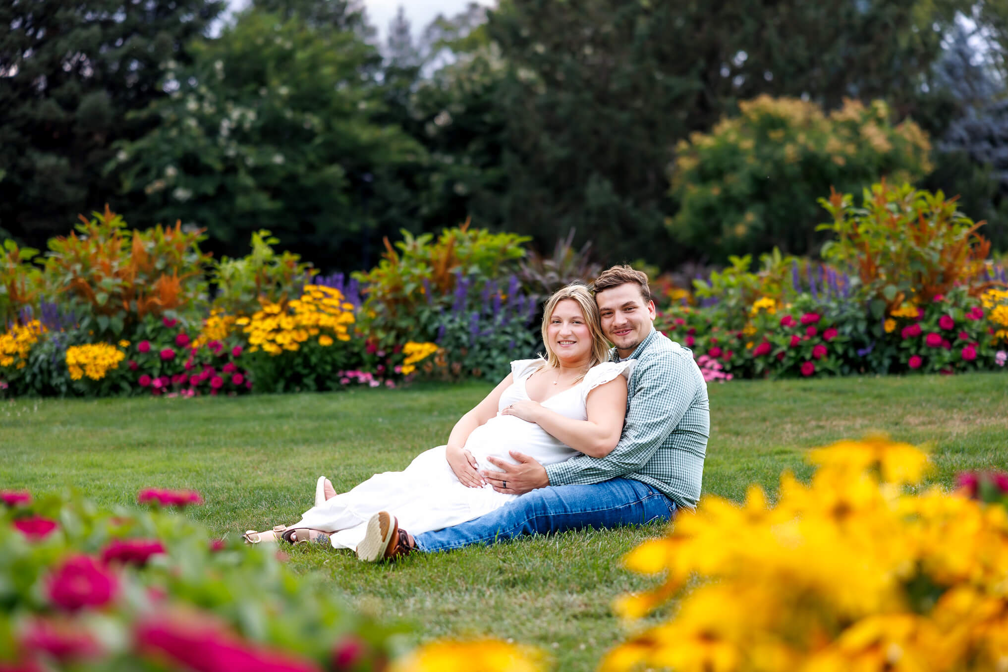 Pregnant mother cradling her baby bump in a white dress during a bright summer maternity session at Hershey Gardens.