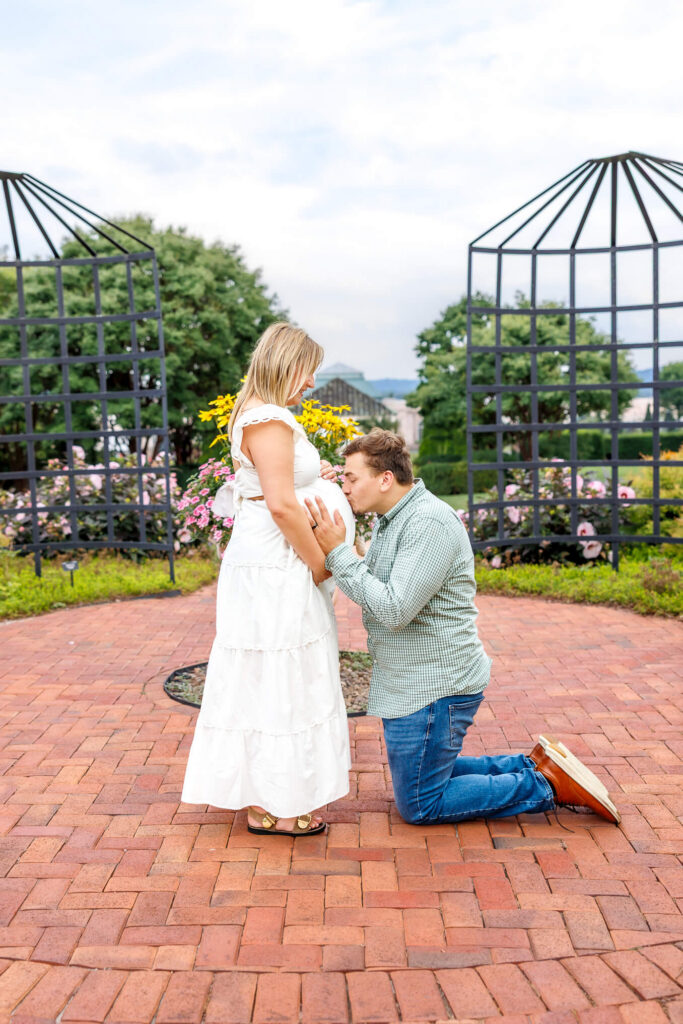 Expectant father kissing his partner’s baby bump during a sweet outdoor maternity portrait.
