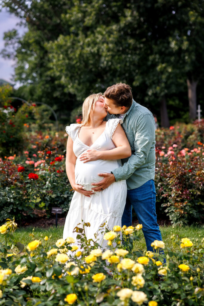Expecting couple kissing in a colorful rose garden during their summer maternity session at Hershey Gardens.