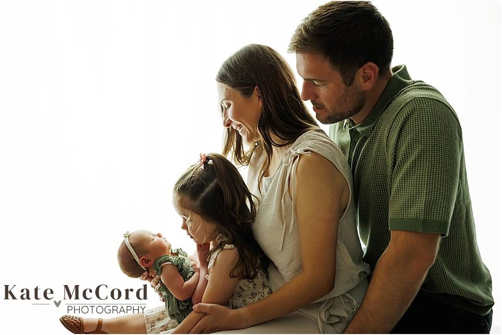 Parents and big sister cuddling their newborn baby girl during a warm, natural family newborn portrait.