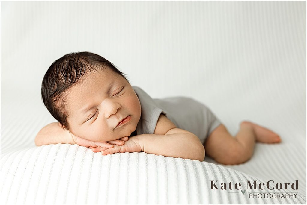 Sleeping newborn baby boy posed on his tummy in a soft gray outfit during a simple studio newborn session.