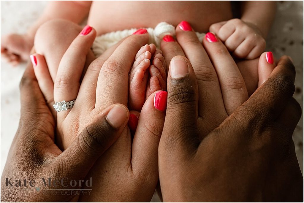 Close-up of a newborn baby’s tiny feet surrounded by their parents’ hands during a newborn photography session.