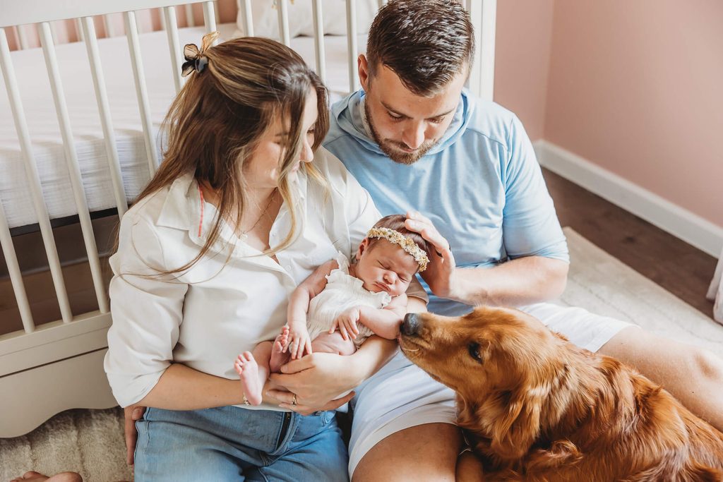 Mom, dad, newborn baby girl, and their first baby golden retriever all snuggling on the nursery floor