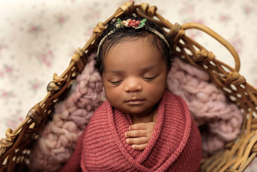 Newborn baby girl wrapped in a dusty rose blanket with a floral headband during a studio newborn session.